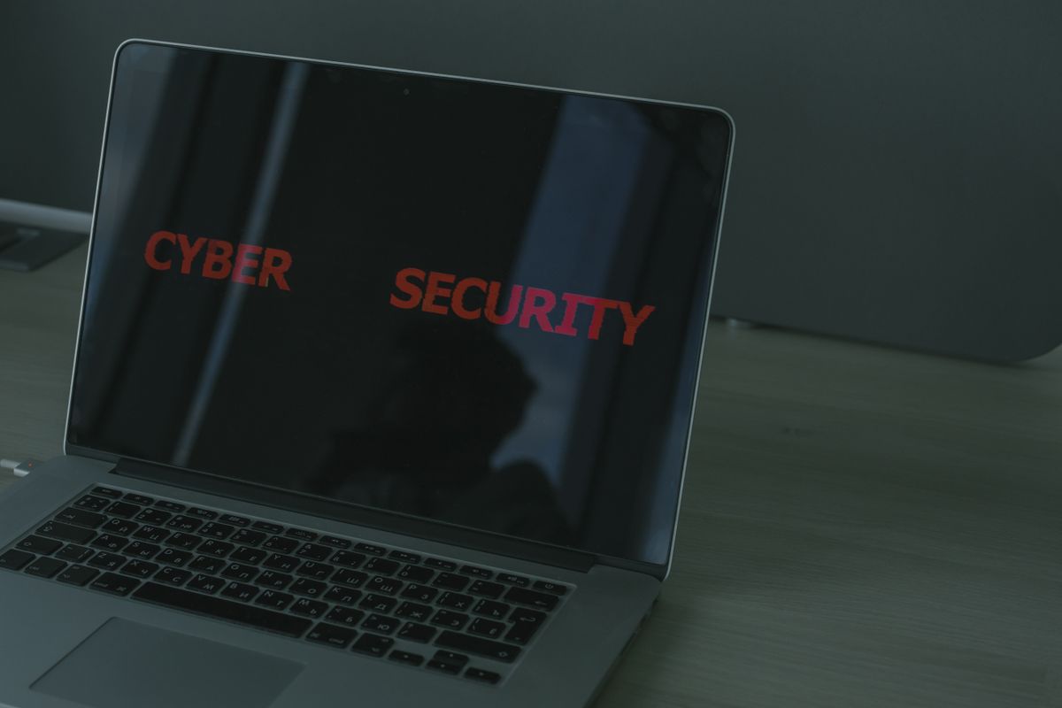 暗い室内で、CYBER SECURITYと赤い文字を表示したノートパソコンが机に置かれている